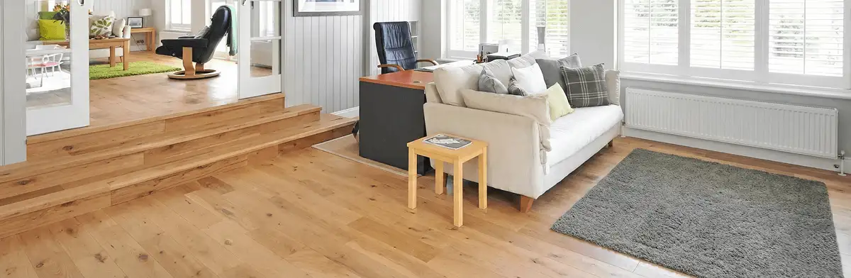 A modern living room with professionally installed laminate flooring, a beige sofa, a small side table, a gray rug, and large windows with white shutters in Orlando, FL
